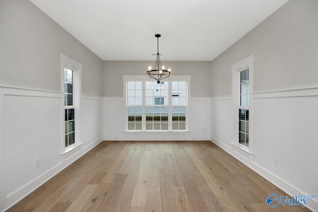 unfurnished dining area featuring an inviting chandelier, plenty of natural light, light wood-style floors, and a wainscoted wall