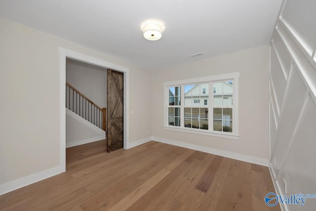 unfurnished room with visible vents, stairway, baseboards, and wood finished floors