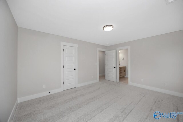 unfurnished bedroom featuring light colored carpet, baseboards, and ensuite bathroom