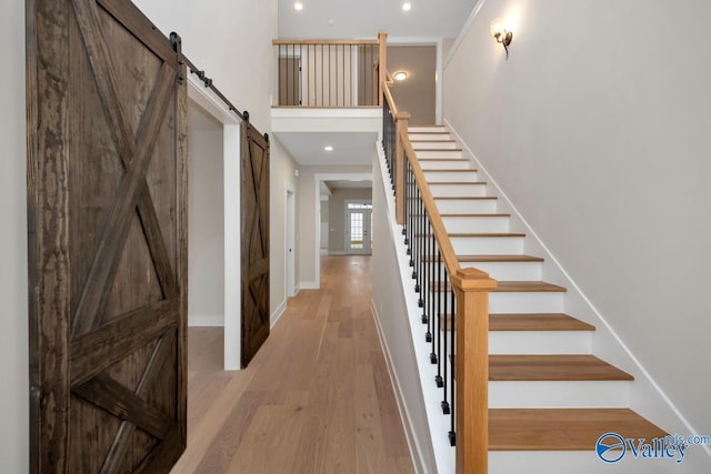 foyer entrance featuring a barn door, baseboards, light wood-style flooring, stairway, and a high ceiling