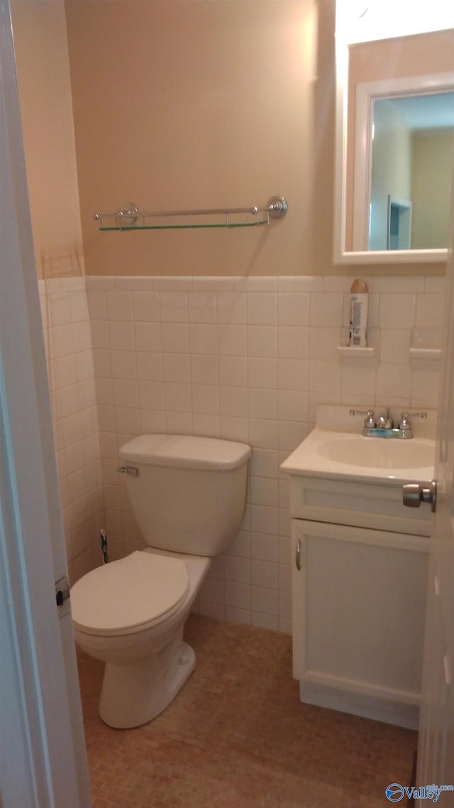 bathroom featuring tile walls, wainscoting, toilet, and vanity