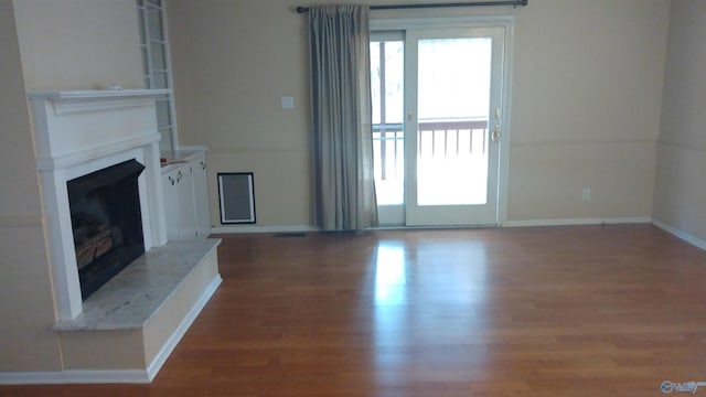 unfurnished living room featuring wood finished floors, a fireplace with raised hearth, and baseboards