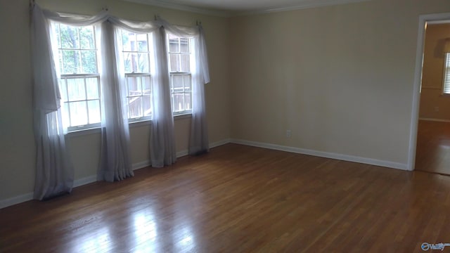 spare room with baseboards, wood finished floors, and crown molding