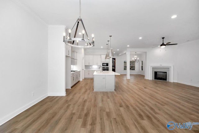 kitchen featuring pendant lighting, black microwave, light hardwood / wood-style floors, an island with sink, and white cabinets