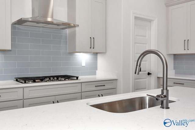 kitchen with light stone counters, sink, stainless steel gas cooktop, and wall chimney range hood