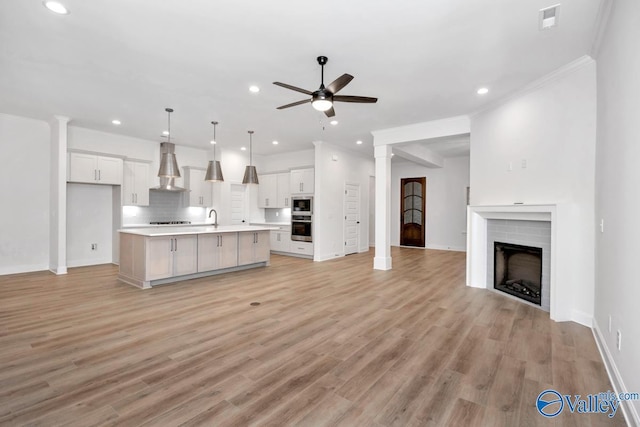 unfurnished living room featuring sink, a fireplace, ceiling fan, and light hardwood / wood-style floors