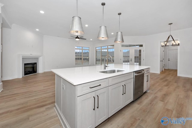 kitchen featuring sink, white cabinetry, stainless steel dishwasher, pendant lighting, and a kitchen island with sink