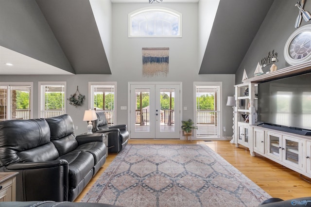 living area with high vaulted ceiling, a wealth of natural light, french doors, and light wood-style floors