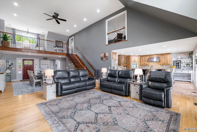 living room featuring ceiling fan, light wood finished floors, high vaulted ceiling, stairs, and recessed lighting