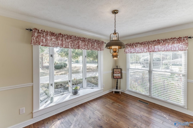 unfurnished dining area featuring a textured ceiling, ornamental molding, and hardwood / wood-style flooring