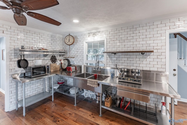 kitchen featuring a textured ceiling, dark hardwood / wood-style floors, crown molding, stainless steel counters, and brick wall