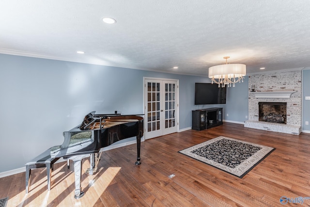 living room featuring hardwood / wood-style floors, a chandelier, crown molding, a brick fireplace, and french doors