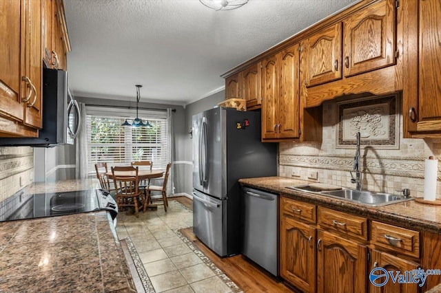 kitchen featuring stainless steel appliances, a sink, backsplash, brown cabinets, and crown molding