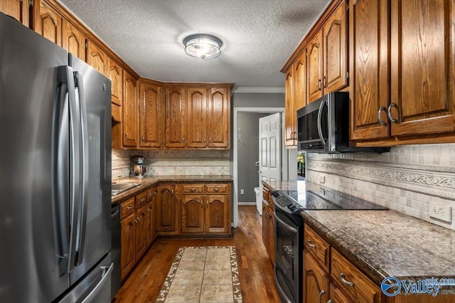 kitchen featuring dark wood finished floors, dark countertops, tasteful backsplash, brown cabinetry, and appliances with stainless steel finishes