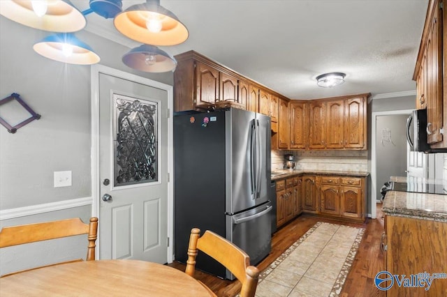 kitchen with stainless steel appliances, tasteful backsplash, wood finished floors, crown molding, and brown cabinetry