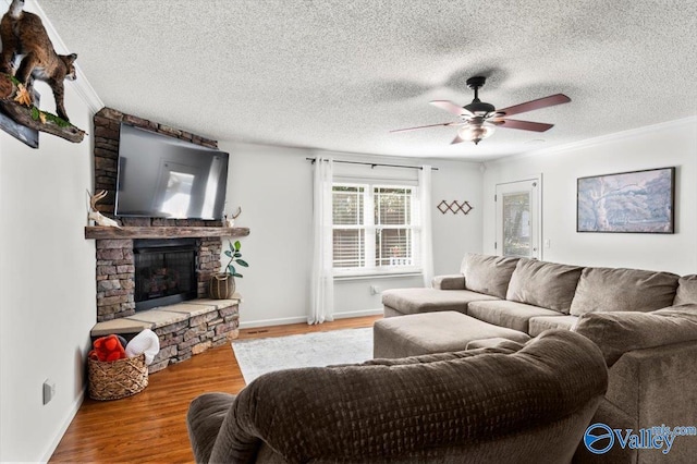 living room with a ceiling fan, wood finished floors, a fireplace, baseboards, and ornamental molding