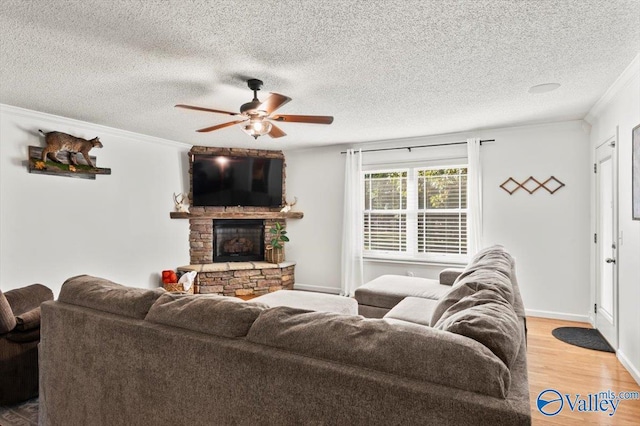 living area with light wood finished floors, a ceiling fan, crown molding, a fireplace, and a textured ceiling