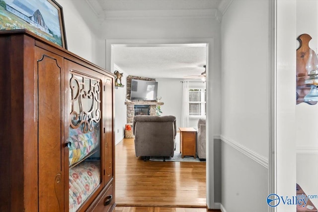 corridor featuring light wood-style flooring, a textured ceiling, and ornamental molding