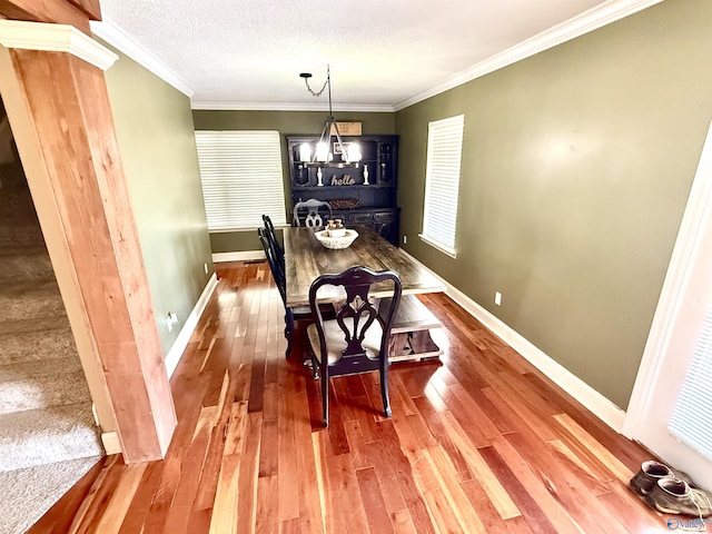 dining area with baseboards, wood-type flooring, a textured ceiling, and ornamental molding