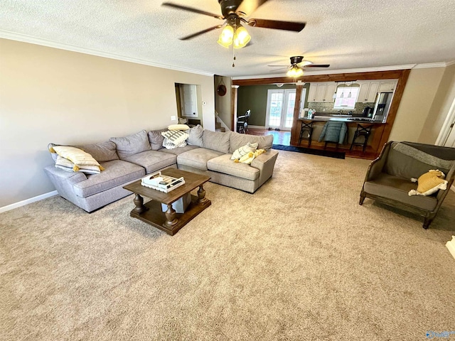 living room featuring a ceiling fan, a textured ceiling, crown molding, baseboards, and light colored carpet