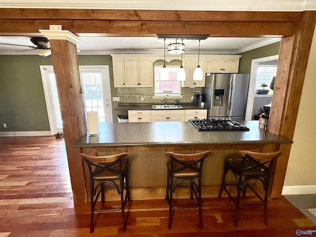 kitchen with dark countertops, tasteful backsplash, stainless steel fridge with ice dispenser, ornamental molding, and a sink