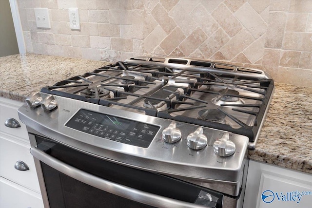 interior details with stainless steel gas range oven, decorative backsplash, white cabinets, and light stone counters