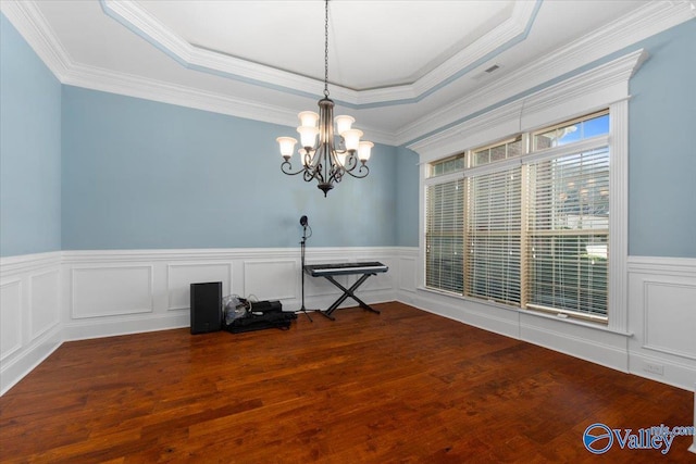 empty room with a raised ceiling, wood-type flooring, crown molding, and an inviting chandelier