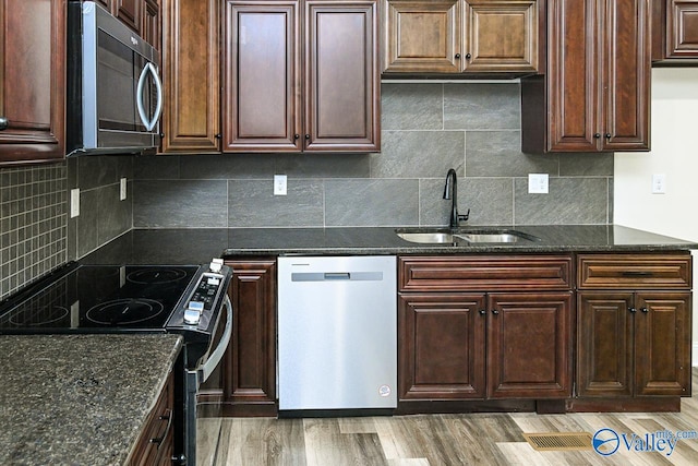 kitchen with sink, stainless steel appliances, dark stone counters, decorative backsplash, and hardwood / wood-style flooring