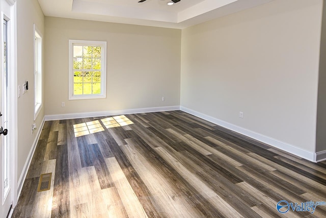 unfurnished room with a tray ceiling, ceiling fan, and dark hardwood / wood-style flooring