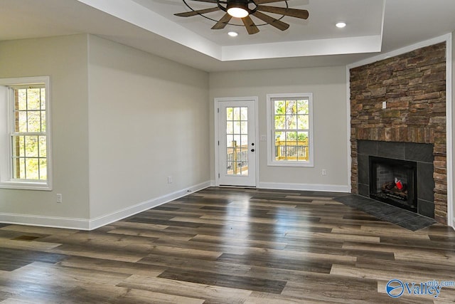 unfurnished living room with a raised ceiling, a stone fireplace, ceiling fan, and dark hardwood / wood-style floors