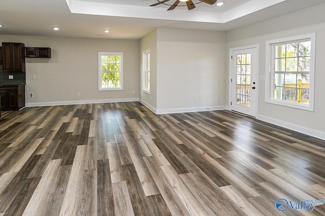 unfurnished living room with a raised ceiling, ceiling fan, and dark wood-type flooring