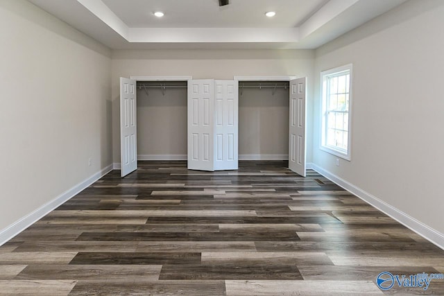 unfurnished bedroom featuring a tray ceiling, multiple closets, and dark hardwood / wood-style flooring