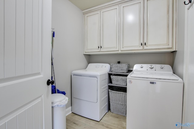 clothes washing area featuring cabinets, washing machine and clothes dryer, and light hardwood / wood-style floors