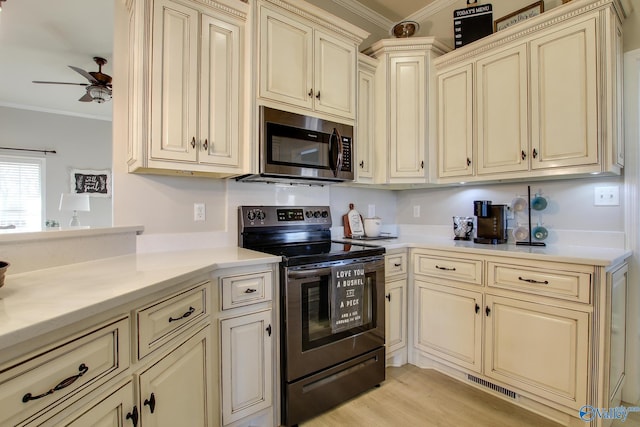 kitchen featuring light wood-type flooring, ornamental molding, ceiling fan, stainless steel appliances, and cream cabinetry