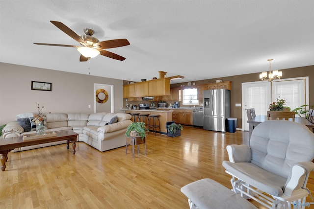 living room with ceiling fan with notable chandelier, light wood-type flooring, and a textured ceiling