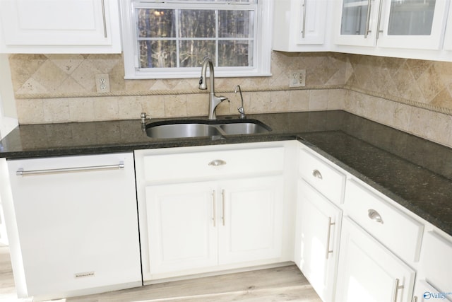 kitchen featuring white dishwasher, sink, dark stone counters, and white cabinets