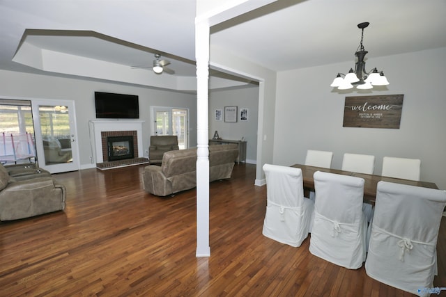 dining space featuring dark hardwood / wood-style floors, a raised ceiling, ceiling fan with notable chandelier, and a brick fireplace