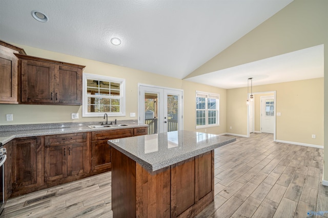 kitchen with lofted ceiling, sink, light hardwood / wood-style flooring, a kitchen island, and light stone counters