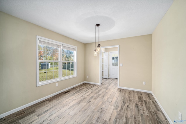 unfurnished dining area featuring a chandelier, light hardwood / wood-style floors, and a textured ceiling