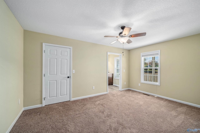 unfurnished bedroom featuring connected bathroom, ceiling fan, light carpet, and a textured ceiling