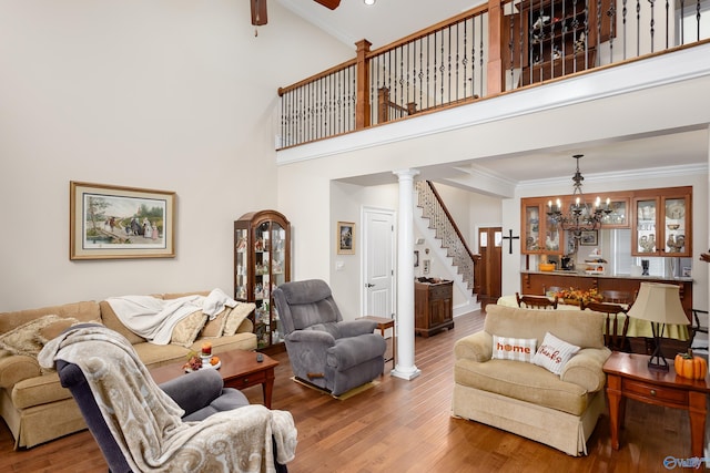 living room featuring ceiling fan with notable chandelier, wood-type flooring, decorative columns, crown molding, and a high ceiling