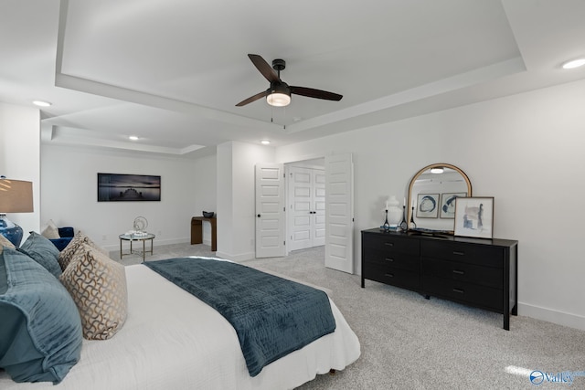 bedroom featuring ceiling fan, a tray ceiling, and light carpet