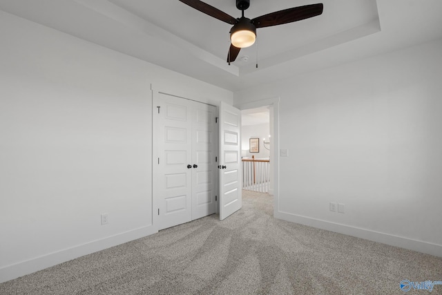 unfurnished bedroom featuring ceiling fan, a tray ceiling, carpet, and a closet