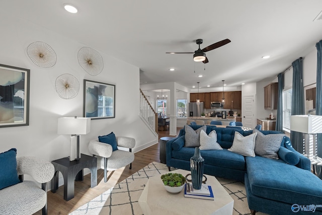 living room featuring ceiling fan with notable chandelier and light wood-type flooring