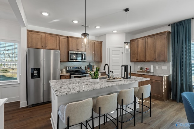 kitchen with decorative light fixtures, a center island with sink, appliances with stainless steel finishes, dark hardwood / wood-style floors, and decorative backsplash