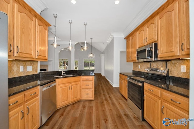 kitchen featuring dark stone counters, crown molding, a sink, light wood-style floors, and appliances with stainless steel finishes