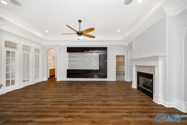 unfurnished living room with a ceiling fan, wood finished floors, arched walkways, a fireplace, and ornamental molding