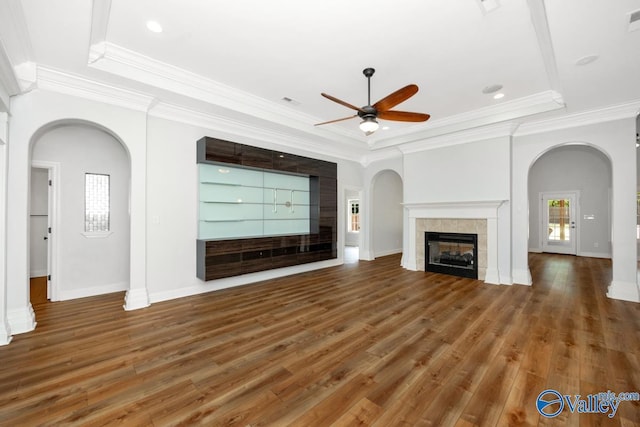 unfurnished living room with arched walkways, a ceiling fan, a tray ceiling, and a fireplace