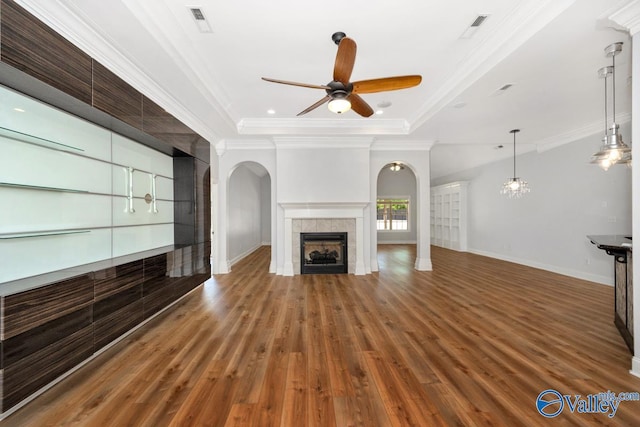 unfurnished living room featuring arched walkways, wood finished floors, ceiling fan, a tile fireplace, and ornamental molding