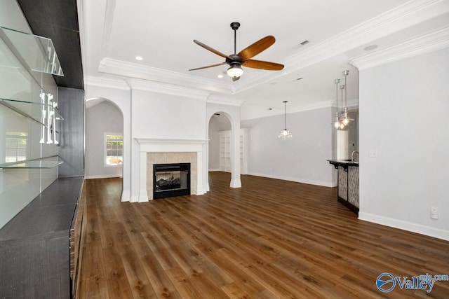 unfurnished living room with ceiling fan, arched walkways, a tray ceiling, and a fireplace